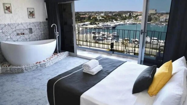 A modern bedroom with a large bed, a bathtub, and a balcony with a marina view. - Sirius Mi Sun Paradise (Cesme)