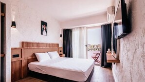 A hotel room with a wooden headboard, a large bed, a flat-screen TV mounted on the wall, and a balcony with a table and chairs. - Sirius Mi Sun Paradise (Cesme)