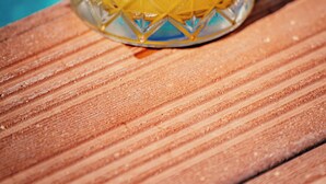A glass with a yellow beverage, mint leaves, and ice cubes, placed on a wooden surface with a blue background. - Sirius Mi Sun Paradise (Cesme)