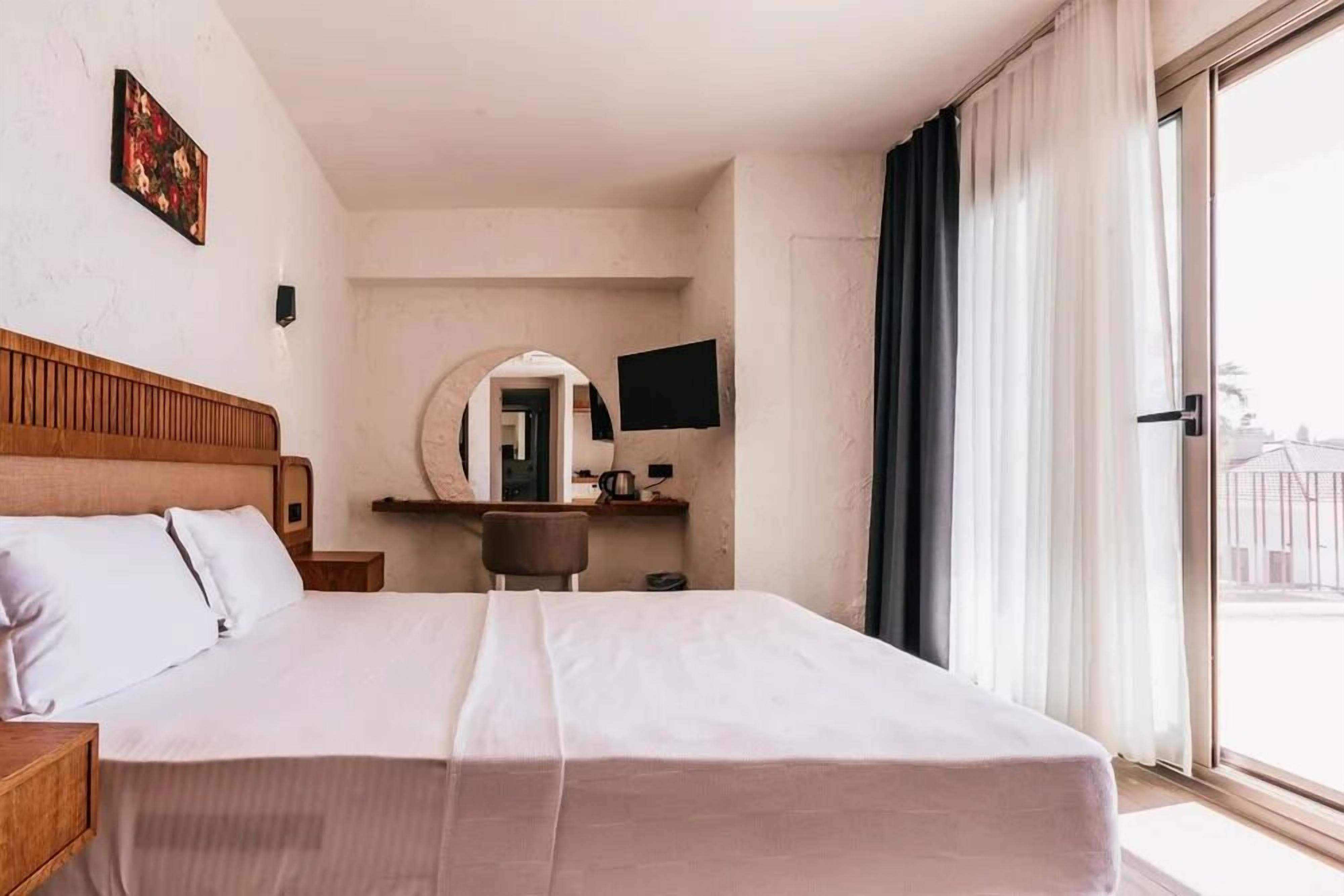 A hotel room with a large bed, a desk with a chair, a television, and a window with curtains.