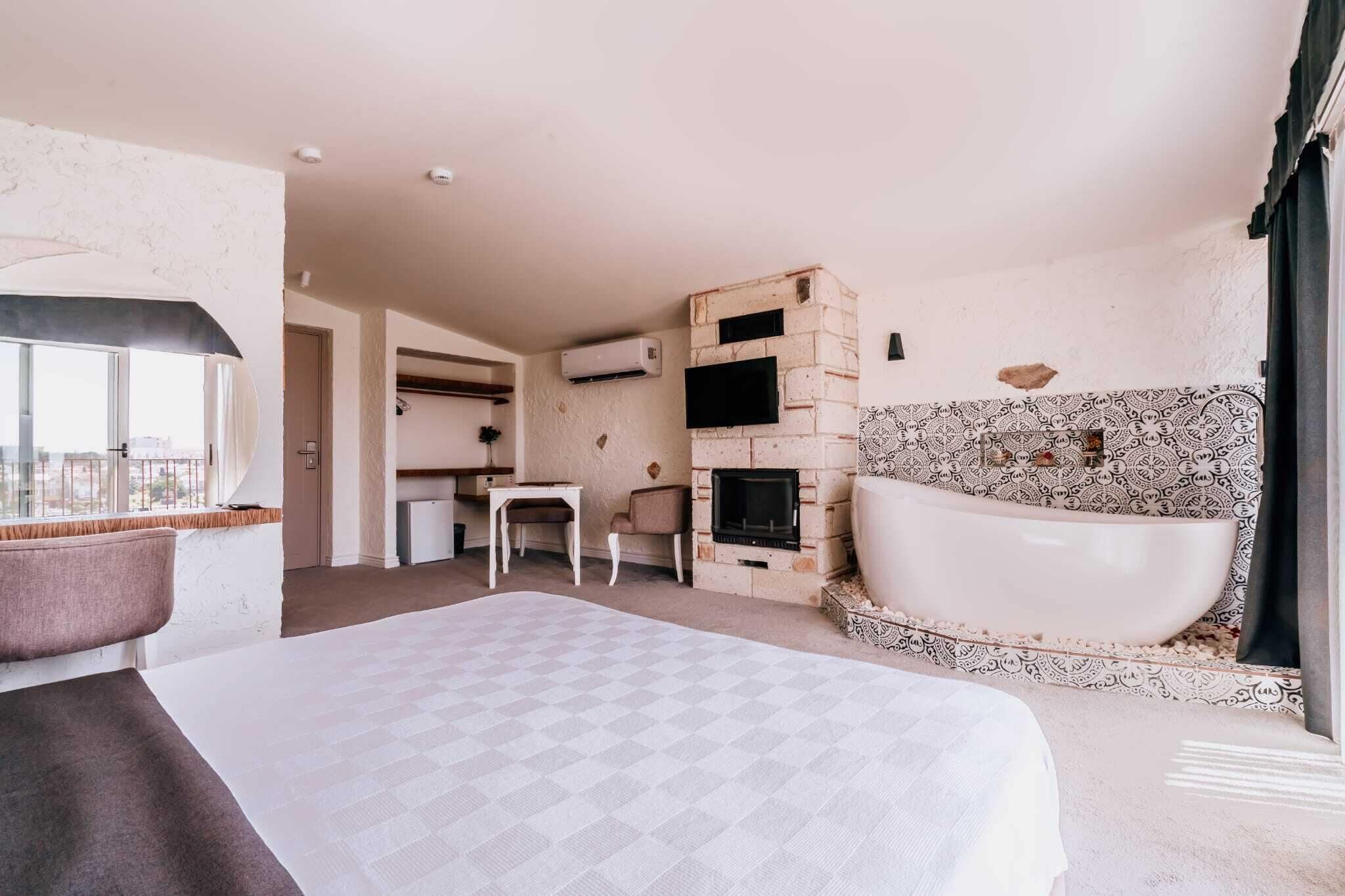 A hotel room with a large bed, a sitting area with a table and chairs, a fireplace, and a bathtub.