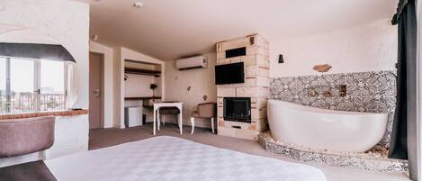 A hotel room with a large bed, a sitting area with a table and chairs, a fireplace, and a bathtub.