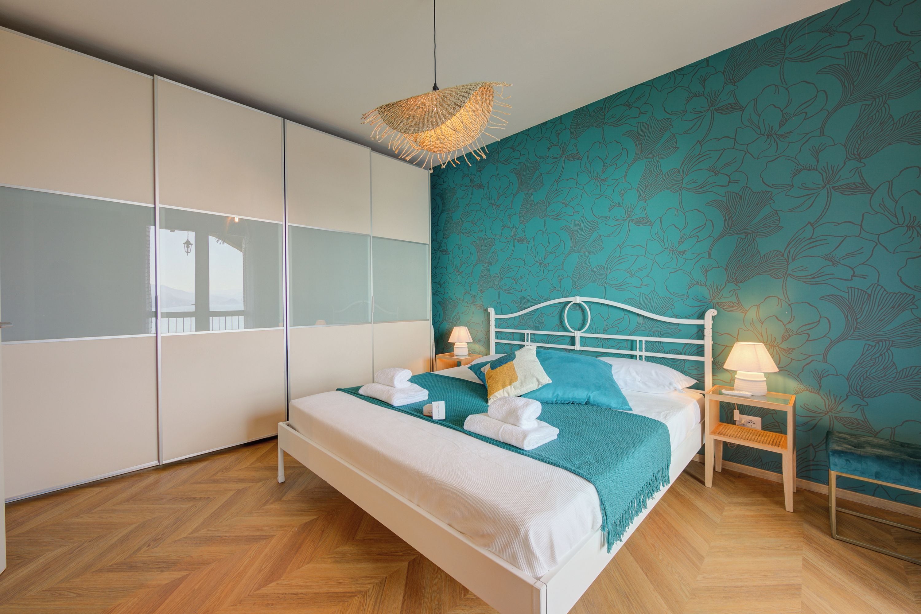 Un dormitorio con cama, mesita de noche, lámpara, armario y pared con estampado floral.