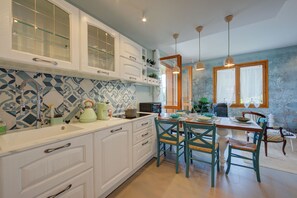 A kitchen with white cabinets, a tiled backsplash, and a dining area with a wooden table and chairs. - Pandora Lake View Stresa and Beach (Stresa)