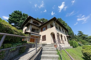 A multi-story building with a staircase leading to the entrance, surrounded by greenery and trees. - Pandora Lake Maggiore View and Private Beach (Stresa)