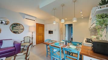 Un espace de vie compact comprenant un coin repas, une cuisine et un coin salon avec un canapé violet et des chaises à rayures.