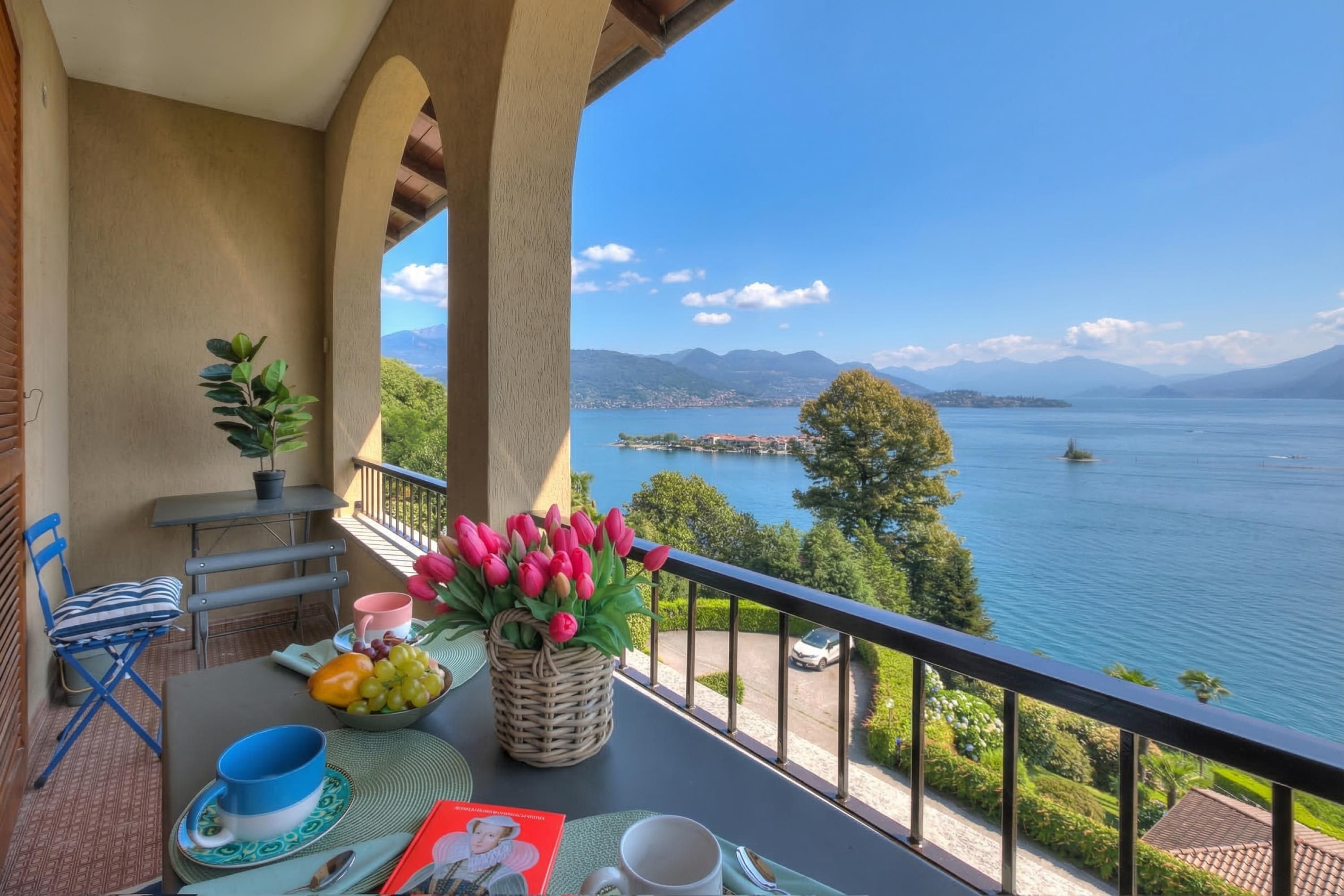 A balcony with a table set for breakfast, a view of a lake, and a mountain range in the distance.