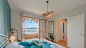 Ett hotellrum med en säng, en balkong med utsikt, en spegel och en dörr som leder till ett annat rum.