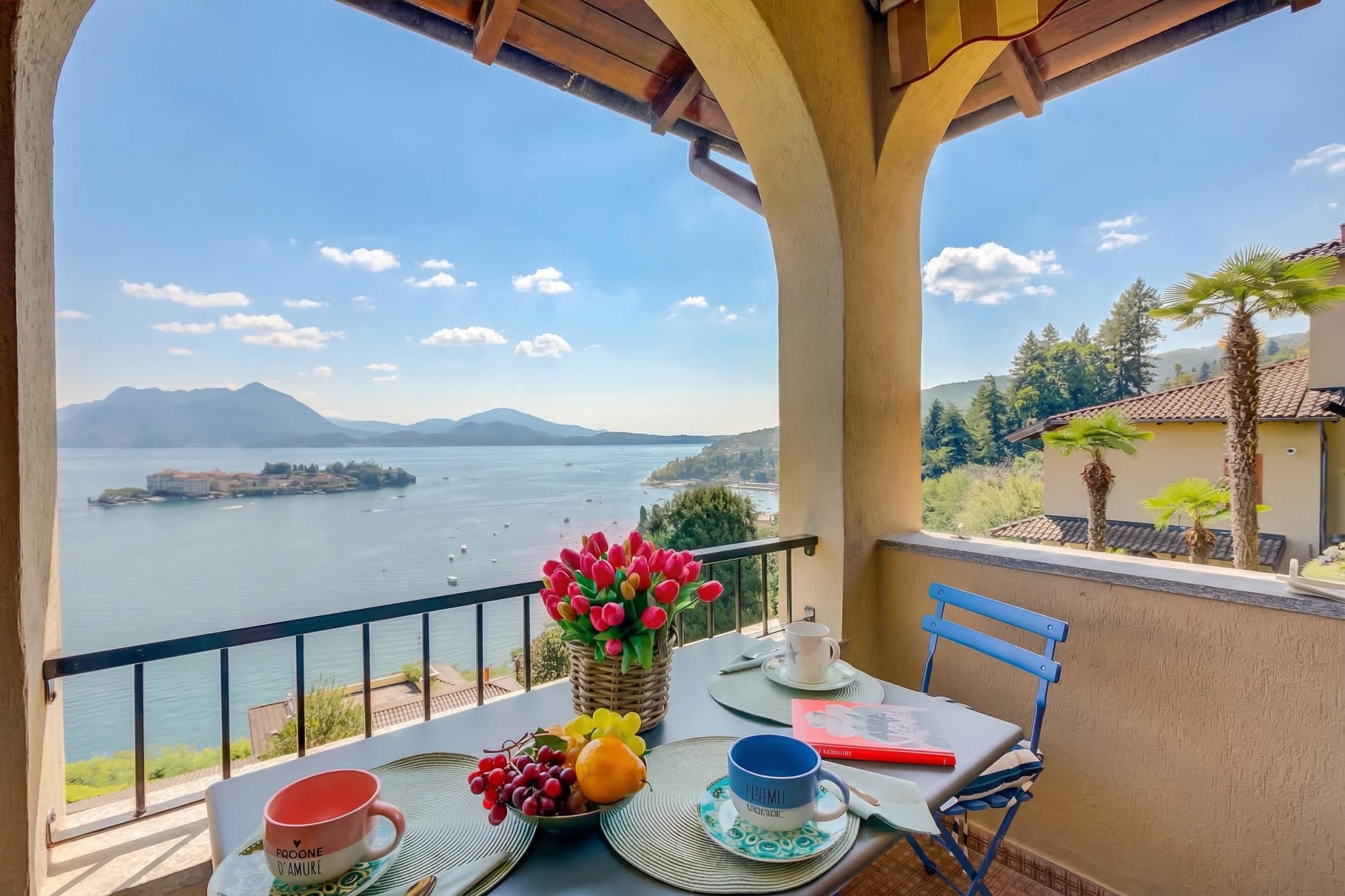 Een balkon met een tafel voor twee, uitzicht op zee, bergen en een gebouw aan de overkant van het water.