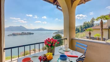 Un balcon avec une table dressée pour deux personnes, une vue sur la mer, les montagnes et un bâtiment situé de l’autre côté de l’eau.