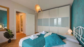 Une chambre à coucher bien rangée, avec un lit, une table de chevet dotée d’une lampe, une plante en pot et un grand miroir.