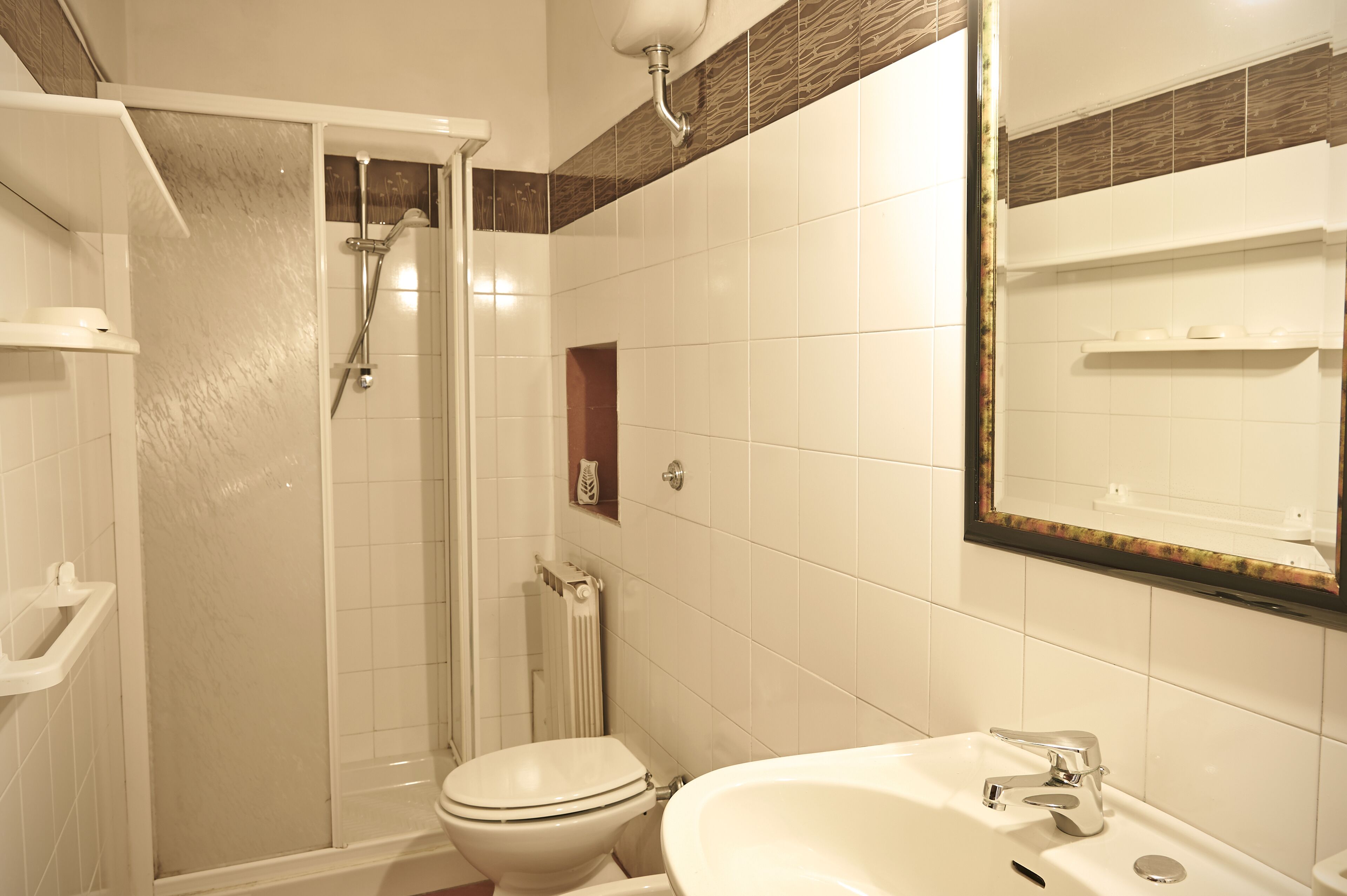 Un bagno con doccia, toilette, lavandino e uno specchio con cornice decorativa.
