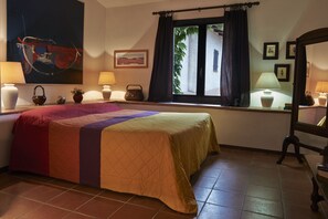 A hotel room with a bed, two bedside lamps, a window with curtains, a wall-mounted painting, and a small table with a lamp. - Agriturismo Bardeggiano (Colle di Val d'Elsa)