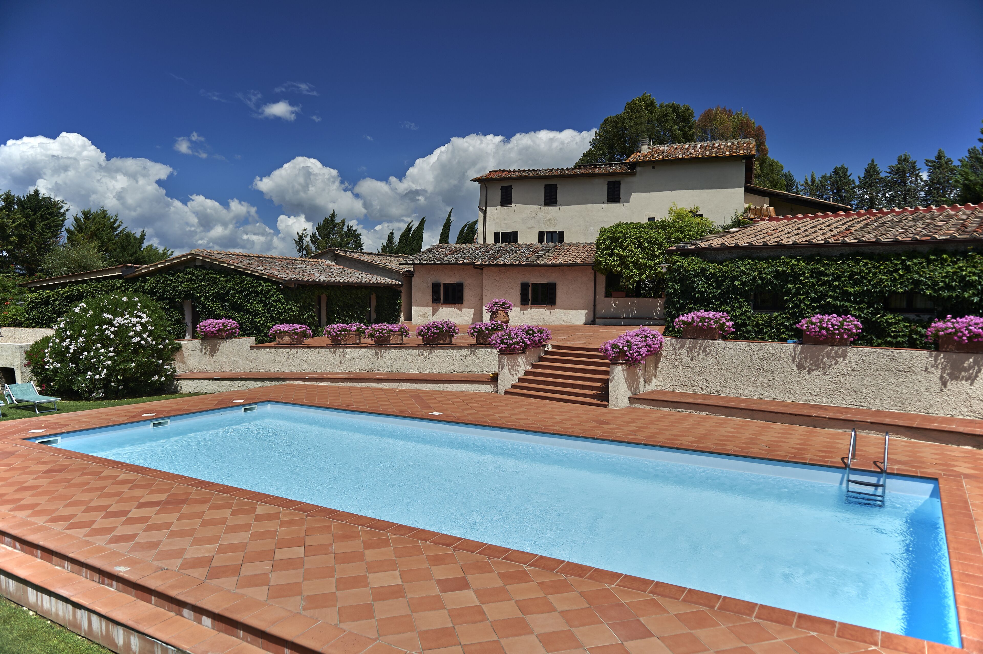 A swimming pool with a tiled deck, a staircase leading to a building, and a clear blue sky.