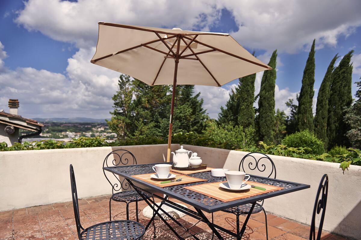 Eine Terrassenanlage im Freien mit einem für Tee gedeckten Tisch, umgeben von Stühlen und einem Sonnenschirm, der Schatten spendet.
