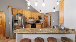 A kitchen with wooden cabinets, stainless steel appliances, granite countertops, and bar stools. - 3br, sleeps 10, Gatlinburg, all the amenities! (Gatlinburg)