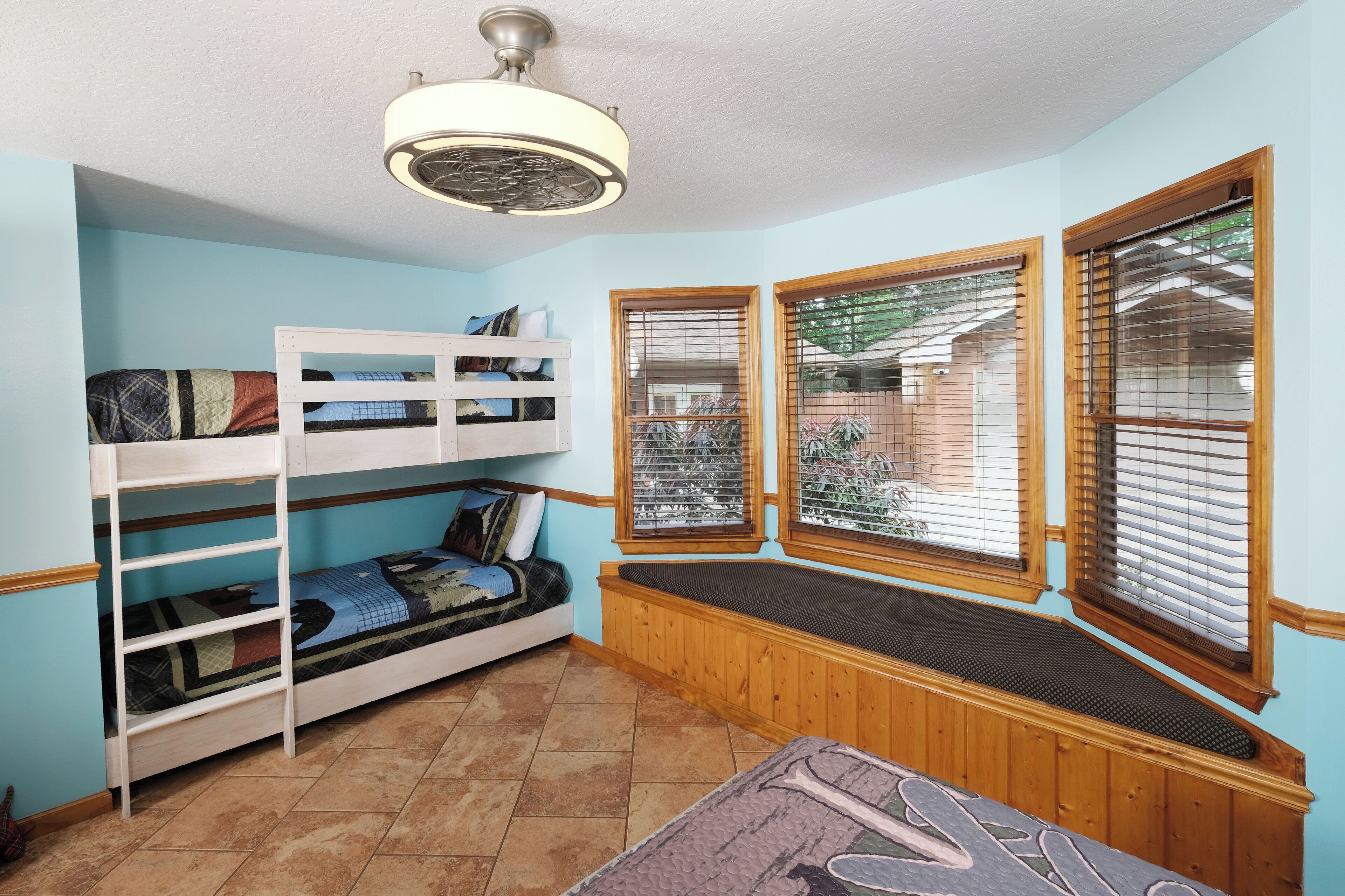 A room with bunk beds, a ceiling fan, and windows with blinds.
