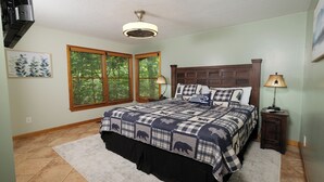 A bedroom with a large bed, two windows with blinds, a ceiling fan, a bedside table with a lamp, and a rug on the floor. - 3br, sleeps 10, Gatlinburg, all the amenities! (Gatlinburg)