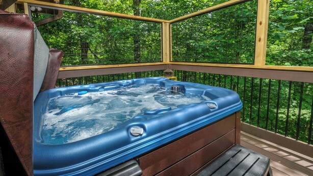 A hot tub on an outdoor deck with a wooden railing and a view of a forested area. - 3br, sleeps 10, Gatlinburg, all the amenities! (Gatlinburg)