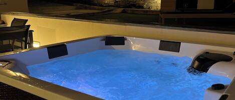 A hot tub with a stone wall backdrop and outdoor seating area.