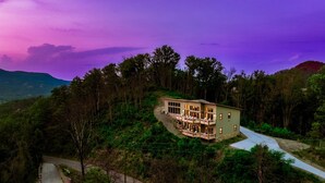 Ein zweistöckiges Haus mit Balkon, umgeben von dichtem Wald und Hügeln.