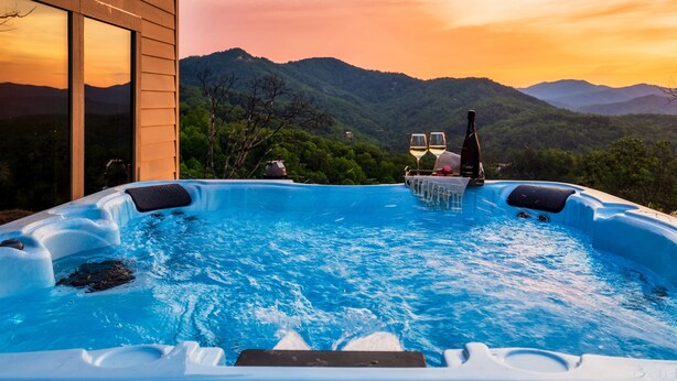 Ein Whirlpool mit Blick auf die Berge, zwei Gläser Weißwein und eine Flasche auf einem Tisch.
