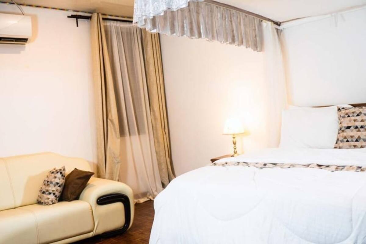 Ett hotellrum med en säng, en soffa, en luftkonditionering och ett fönster med gardiner.