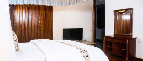 A hotel room with a bed, a television, a wooden wardrobe, and a mirror.