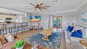 A spacious living area with a wooden dining table, a sofa, and a couch. There is a ceiling fan, a kitchen with a microwave, and a TV displaying a beach scene. - Private heated Pool/Gym/Games/Sauna/Massage Chair (Hernando Beach)