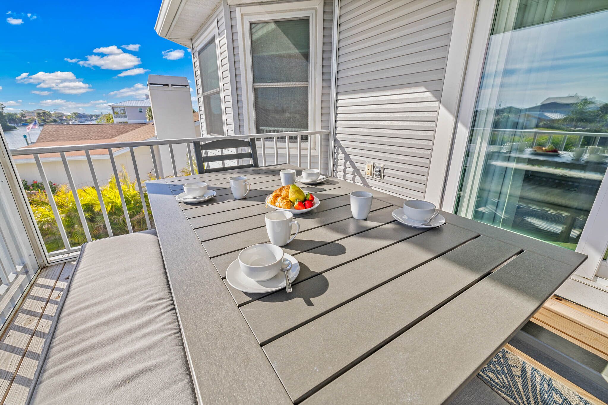 A balcony with a table set for breakfast, including a plate of fruit, cups, and saucers.