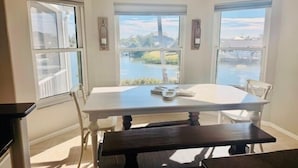 A dining area with a white table and chairs, a dark bench, and large windows offering a view of a body of water and greenery. - Private heated Pool/Gym/Games/Sauna/Massage Chair (Hernando Beach)