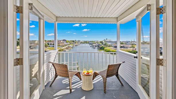 A balcony with wicker chairs and a table, overlooking a river and residential area. - Private heated Pool/Gym/Games/Sauna/Massage Chair (Hernando Beach)