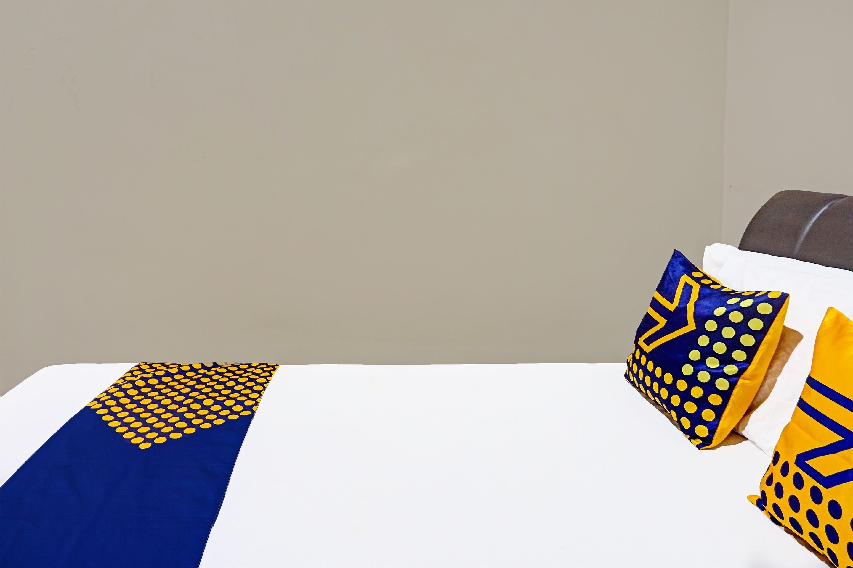 A hotel room with a neatly made bed, two pillows with geometric patterns, and a plain wall.