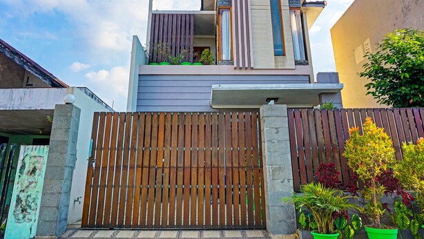Una casa moderna de dos pisos con un portón de madera, un balcón con plantas y un cielo despejado.