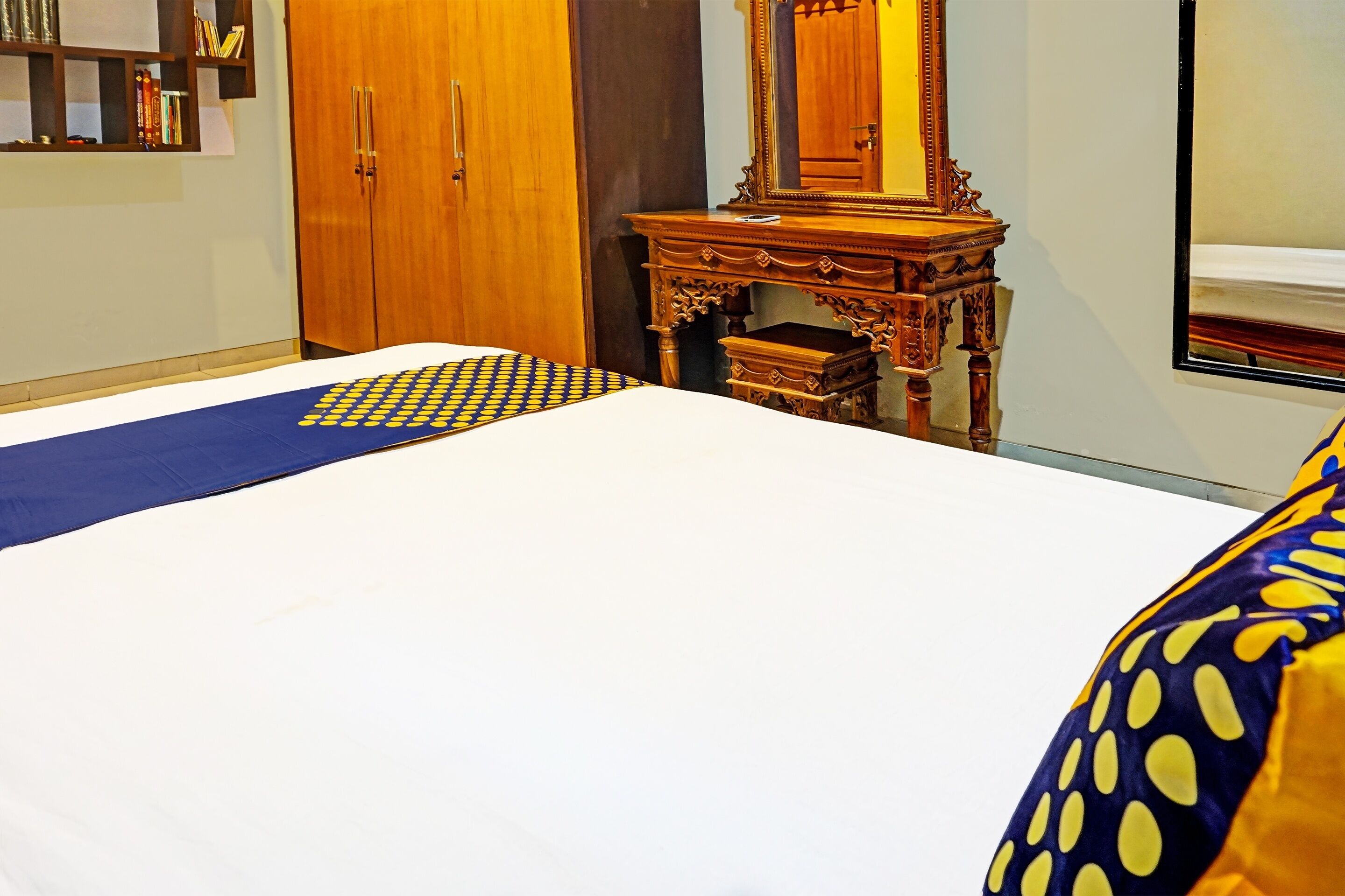 A hotel room with a large bed, a wooden wardrobe, a small wooden dresser, and a mirror.