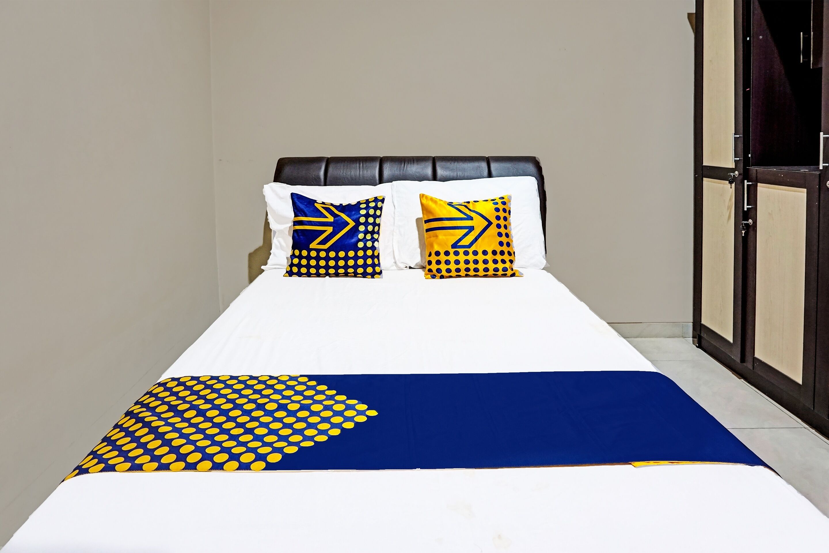 A bed with a white and blue bedspread, two pillows with yellow and blue patterns, and a dark headboard.