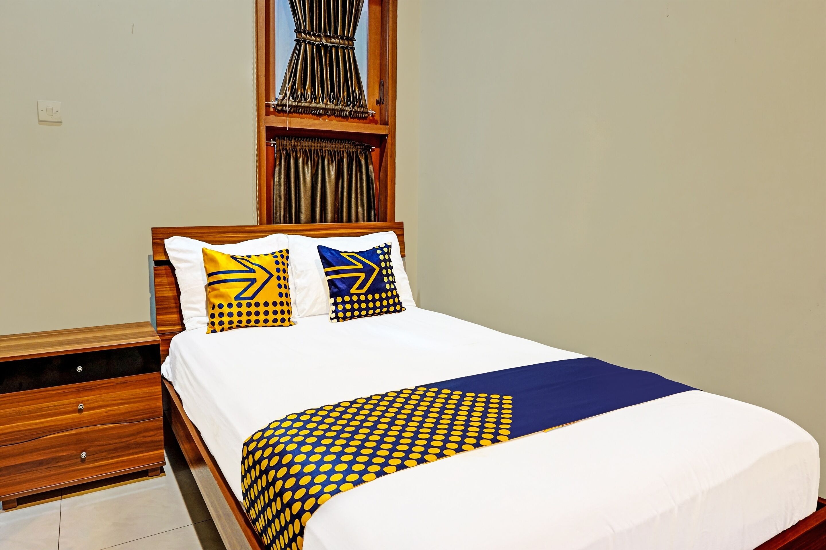 A neatly made bed with a white and blue bedspread, two decorative pillows, and a wooden headboard.