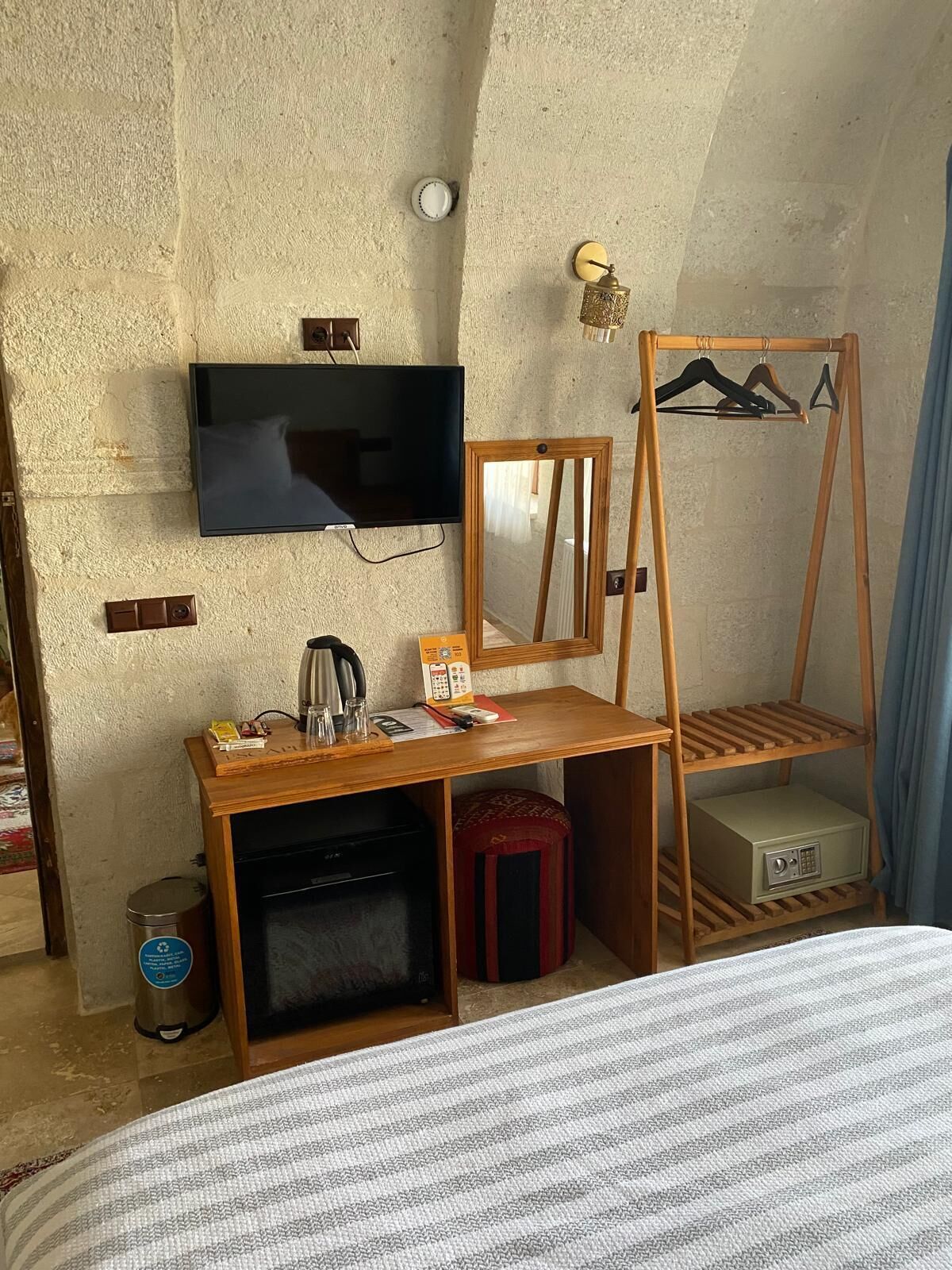 A room with a TV, wooden desk, mirror, clothes rack, and a small safe.