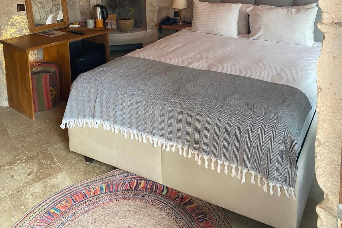 A bedroom with a stone wall, a bed with white bedding, a bedside table with a lamp, and a mirror.