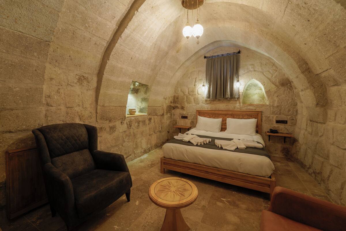 A stone-walled room with a bed, a chair, and a small table.