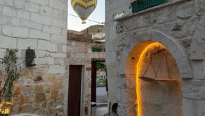 Une rue étroite bordée d’immeubles en pierre, un ballon à air chaud visible au loin et une arche illuminée.
