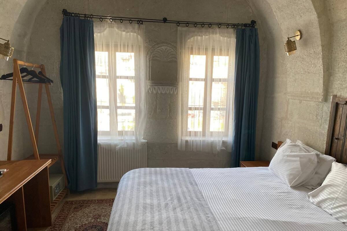 A bedroom with a bed, a wooden bench, a radiator, and a window with curtains.