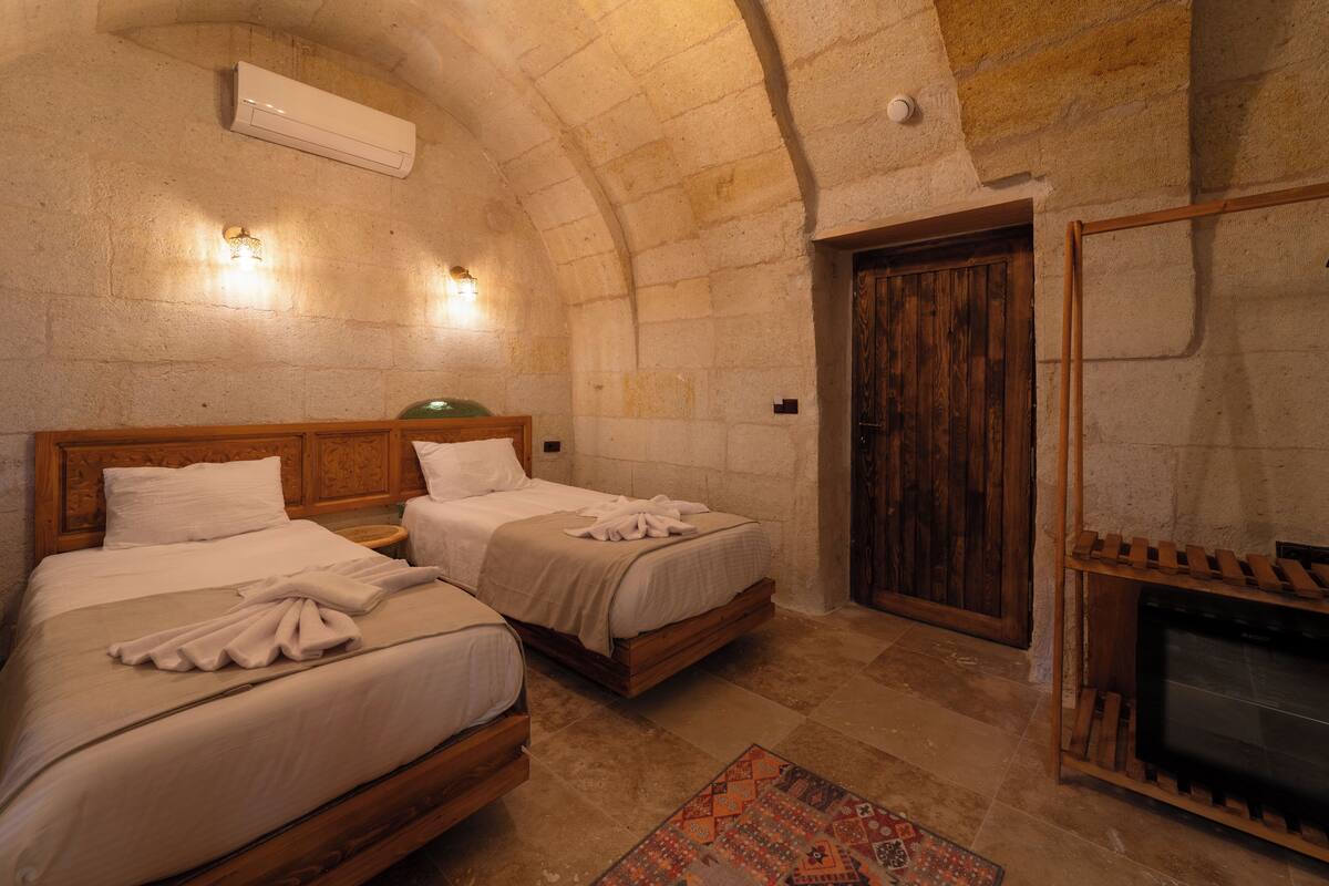 A cozy room with two beds, a fireplace, and a stone wall.