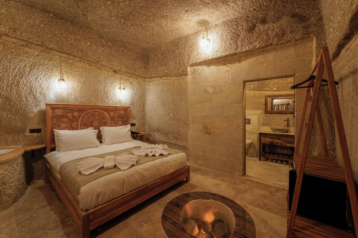 A room with a large bed, a wooden headboard, a small round table with a bowl, and a wooden ladder.