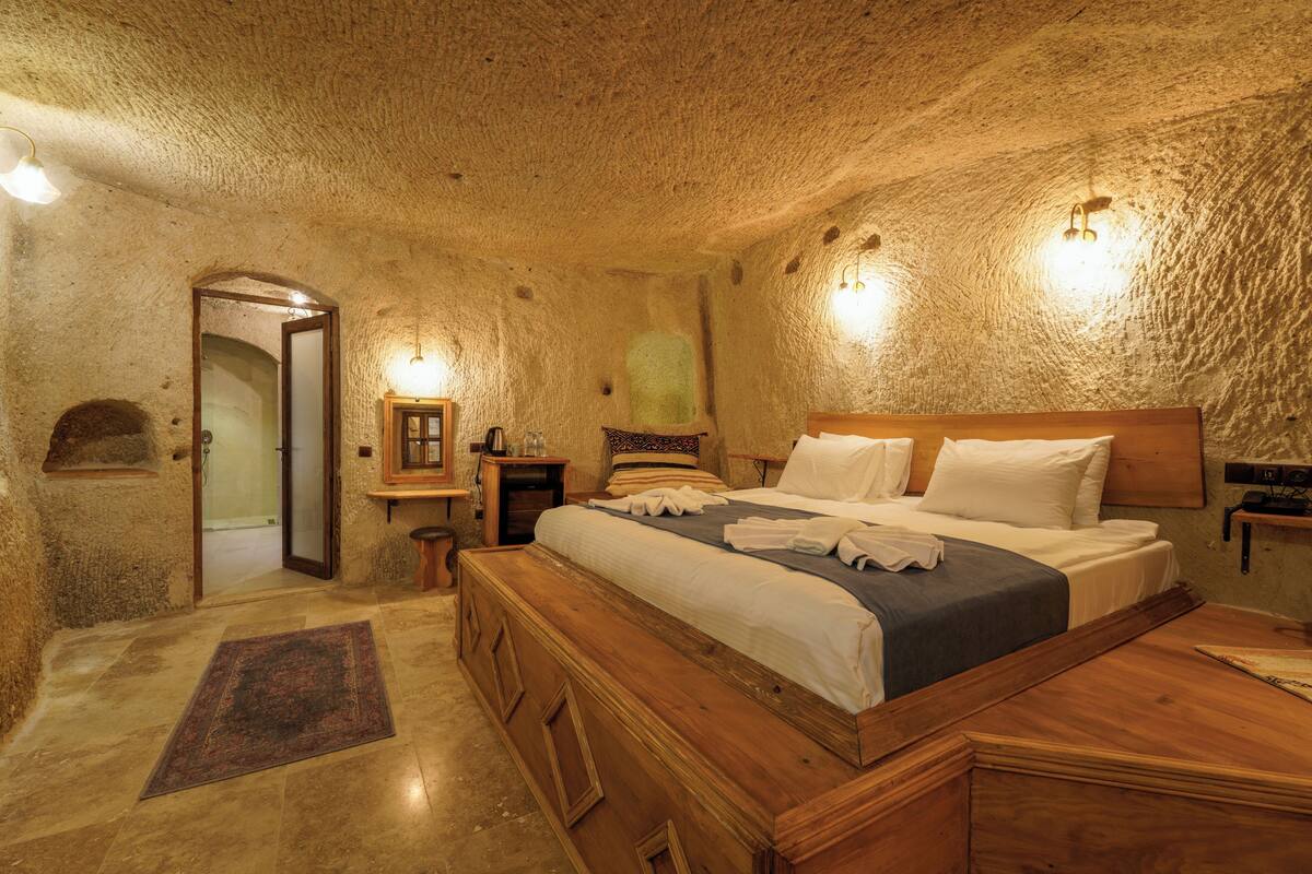 A bedroom with a large wooden bed, a wooden nightstand, a small table, and a wall-mounted shelf.