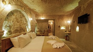 Une chambre aux murs de pierre, avec un lit, des oreillers, une tête de lit en bois, un téléviseur à écran plat et une arche en pierre.