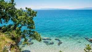 A coastal landscape with clear turquoise waters, rocky shoreline, and lush greenery. - Colourful Seaview Apartment (Kostrena)