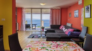 A living room with a sofa, chairs, a table, and a view of the sea through a sliding glass door. - Colourful Seaview Apartment (Kostrena)