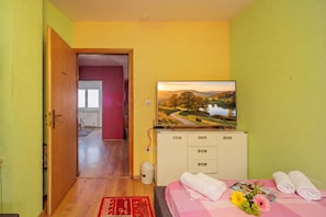 A hotel room with a bed, a television on a cabinet, a red rug, and towels. - Colourful Seaview Apartment (Kostrena)