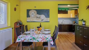 A dining area with a table set for four, a fruit bowl, and a painting of a lion on the wall. - Colourful Seaview Apartment (Kostrena)